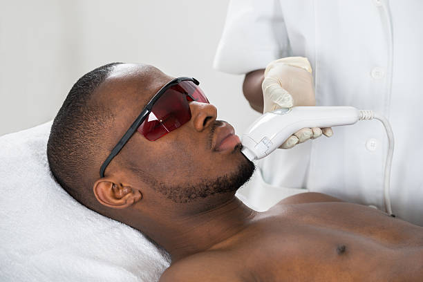 Close-up Of Therapist Giving Laser Epilation Treatment On Young African Man