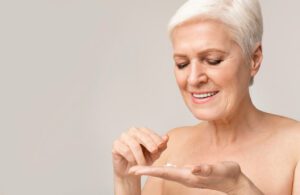 A happy senior woman is applying anti-wrinkle cream as part of her anti-aging skincare routine for better skin health.