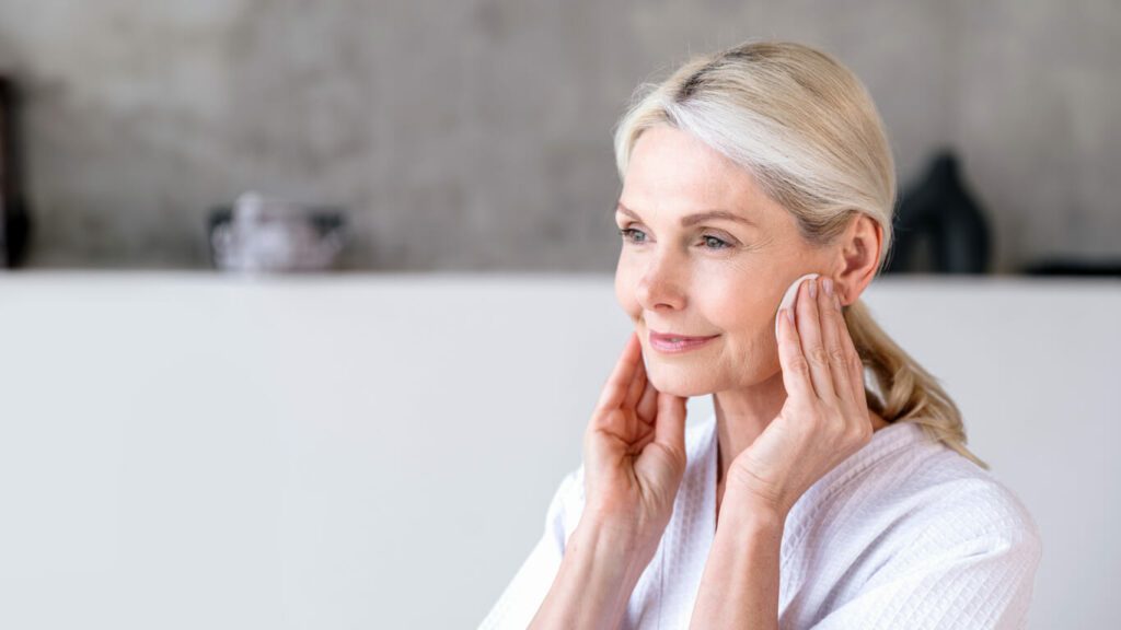 An elderly woman follows a skincare routine and facial treatment for aging skin, cleansing her face with a sponge.