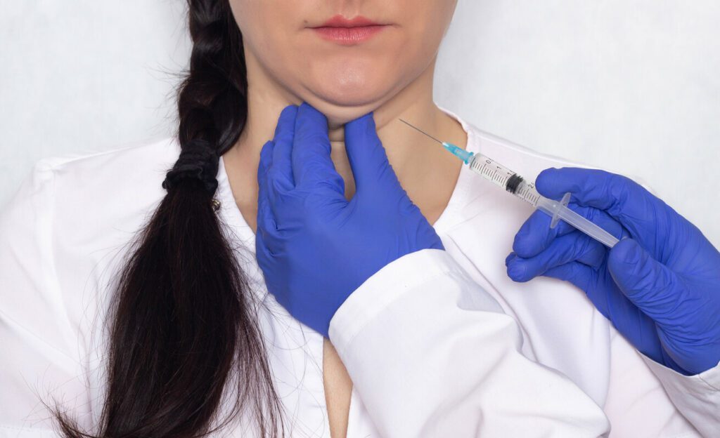 A doctor gives lipolytic injection to a caucasian girl's double chin on a white background,